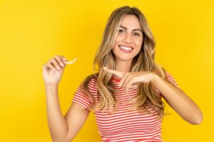 Woman in red and white striped shirt smiling and pointing to Invisalign with yellow background