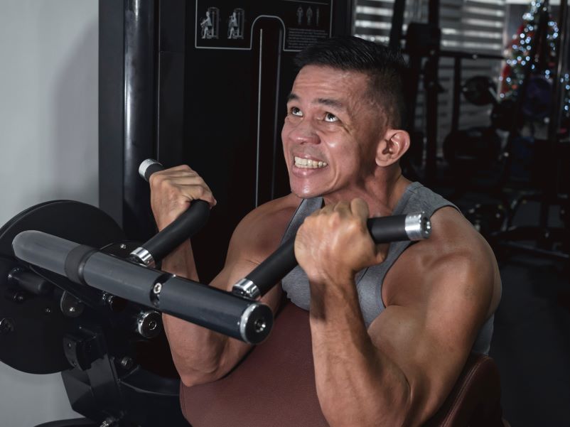 A man gritting his teeth as he lifts weights.