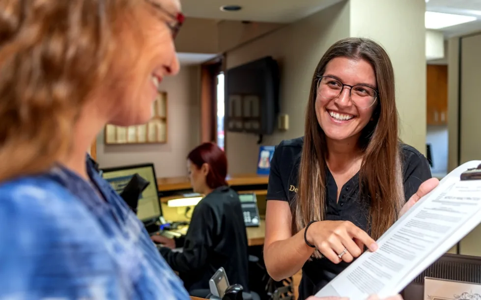 Dental team member showing a patient where to sign paperwork on a clipboard