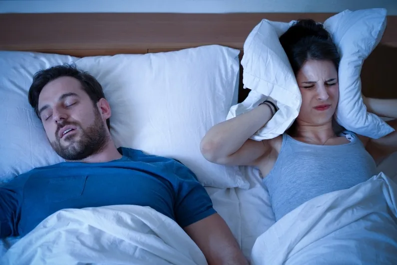 Woman covering her ears with a pillow while a man snores