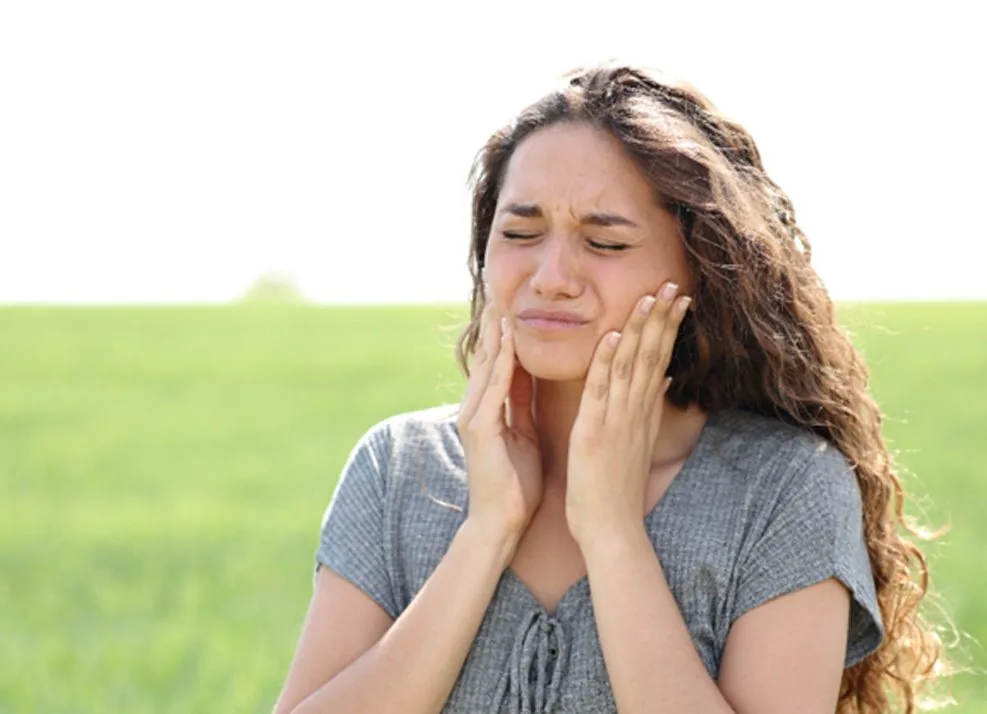 Woman experiencing jaw pain outdoors