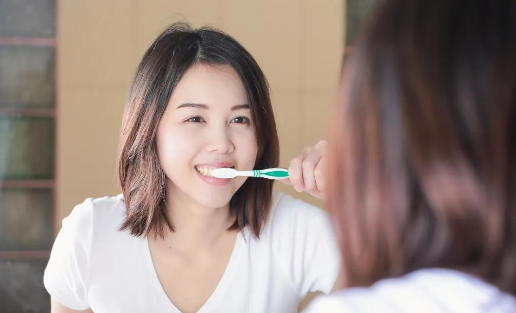 Woman brushing her teeth in front of a bathroom mirror